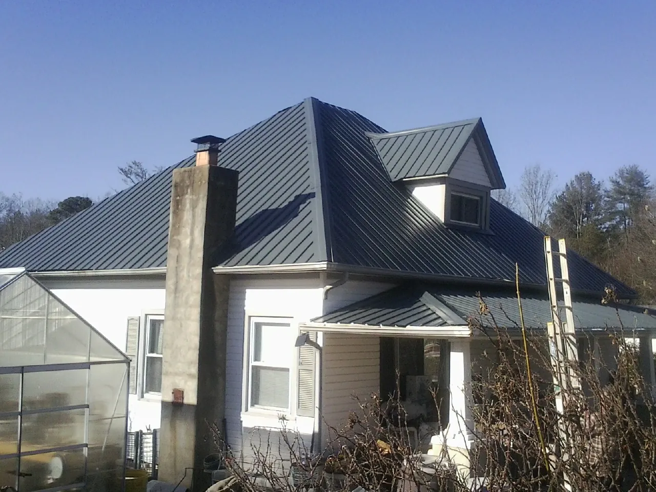 Dark blue standing seam metal roof on a white farmhouse with dormer — Slate & Tile Roof Repair by Roofing Brothers in Water Mill