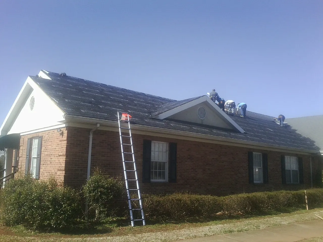 Crew tearing shingles off a brick ranch roof with a ladder set — Emergency Roof Repair work by our crew in Water Mill