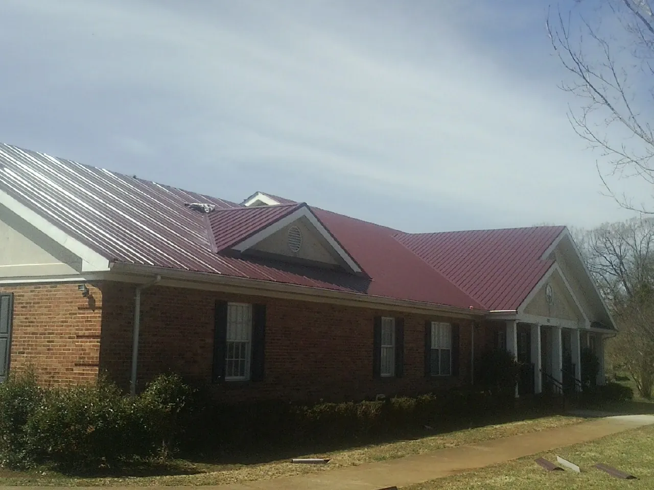 Red metal roof with gabled entries on a long brick building, from a Hail Damage Roof Repair job in Water Mill