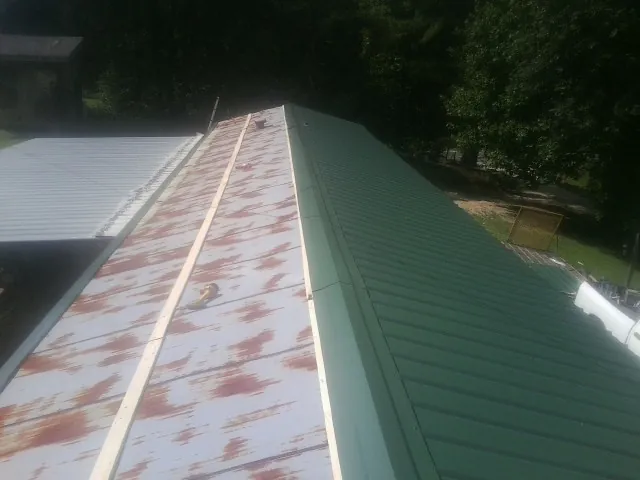 Old rusted panels beside newly installed green metal roofing — Wind Damage Roof Repair by Roofing Brothers in Water Mill