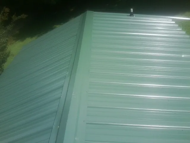 New green metal panels meeting at the ridge of a roof — Flat Roof Repair work by our crew in Water Mill