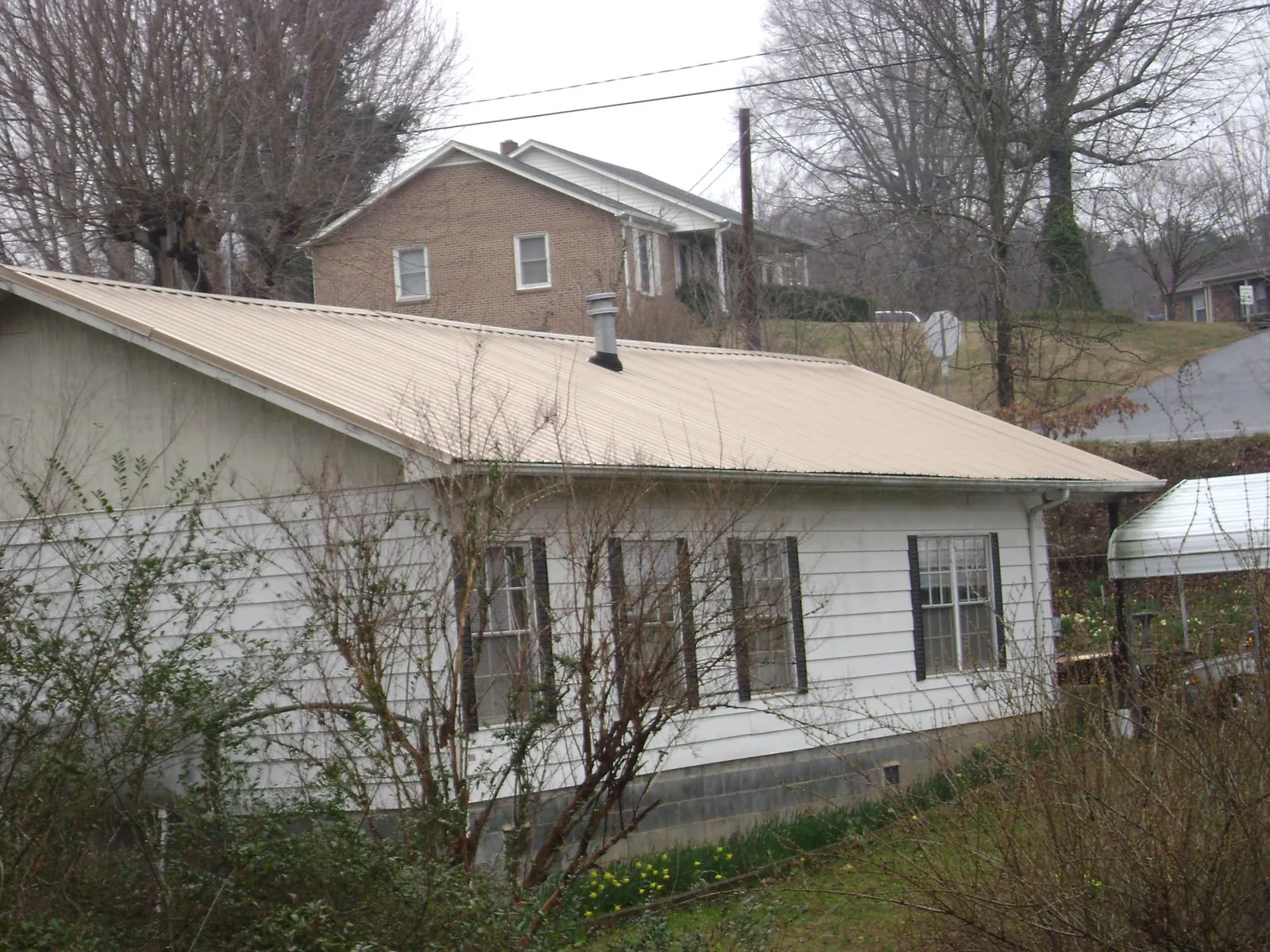Tan metal roof on a white sided house set into a hillside in Water Mill