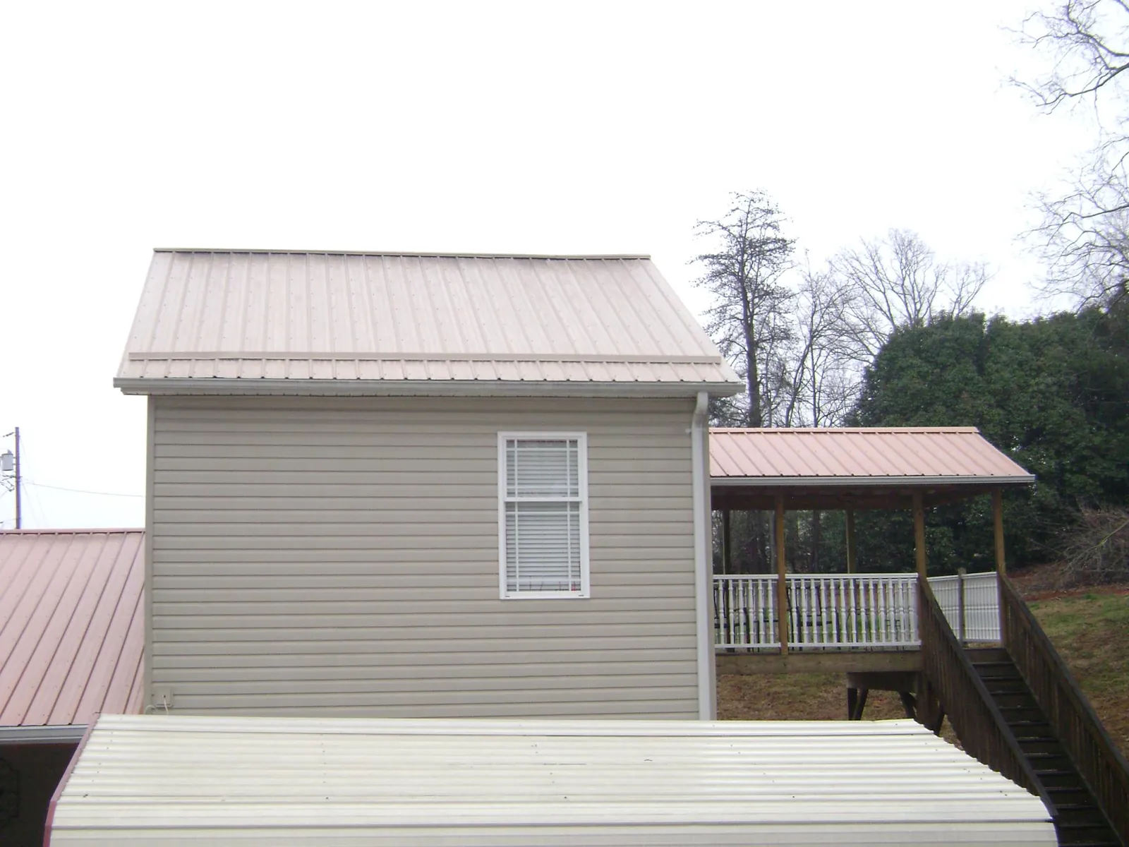 Tan metal roofs on a two story addition and attached porch, from a Roof Replacement job in Water Mill